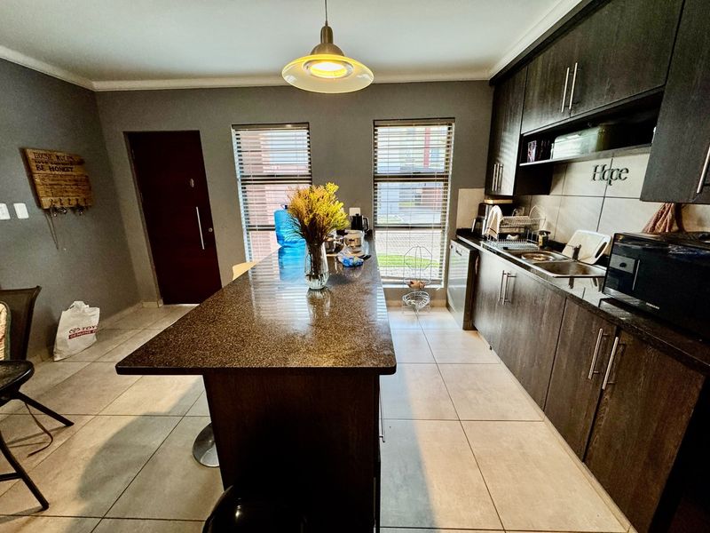 Modern kitchen featuring dark wood cabinetry, granite countertops, a central breakfast island, and tiled flooring with natural light from dual windows.