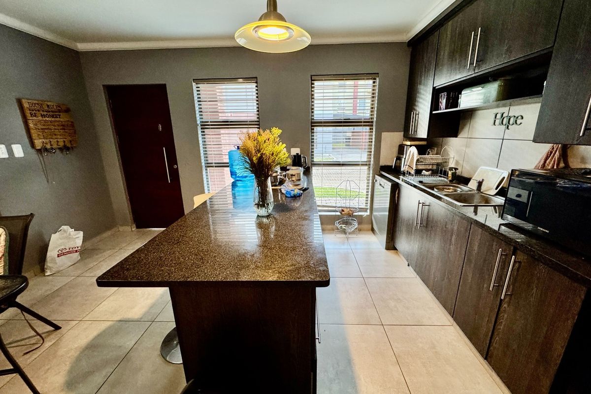 Modern kitchen featuring dark wood cabinetry, granite countertops, a central breakfast island, and tiled flooring with natural light from dual windows.