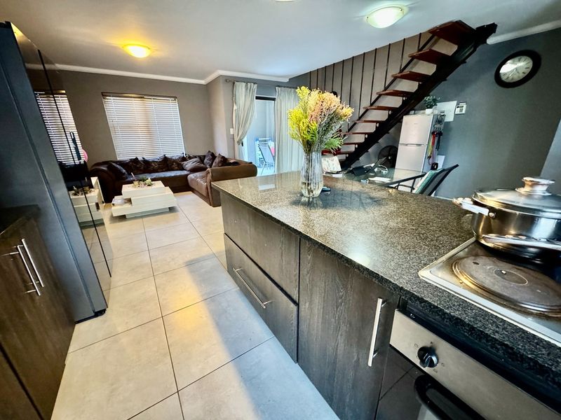 Open-plan living area featuring a modern kitchen with a granite island, built-in oven, hob, and a staircase leading to the upper level.