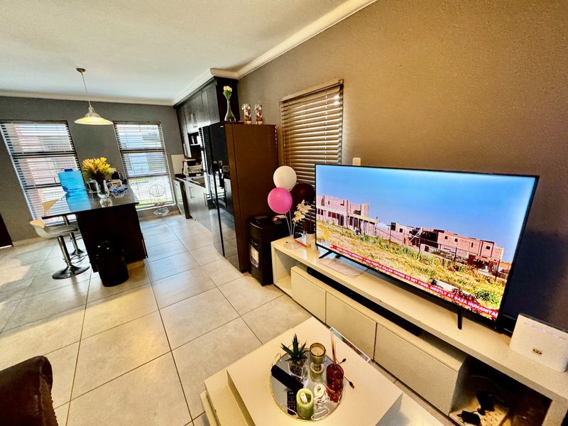 An open-plan living and kitchen area featuring tiled flooring, dark cabinetry, and large windows with venetian blinds, creating a functional and connected living space.