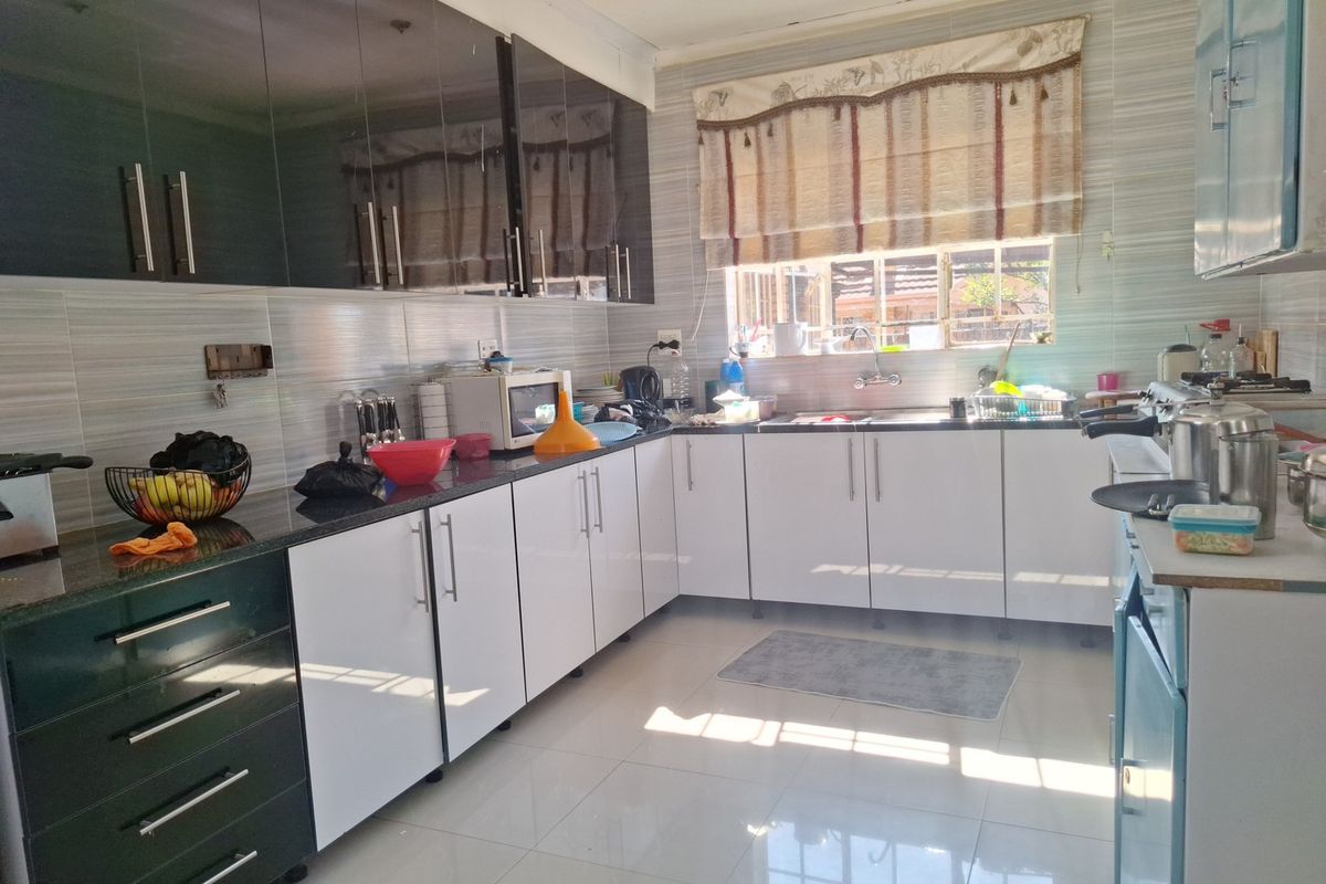 A functional kitchen featuring contrasting dark and white cabinetry, granite countertops, tiled backsplash, and tiled flooring with ample natural light.