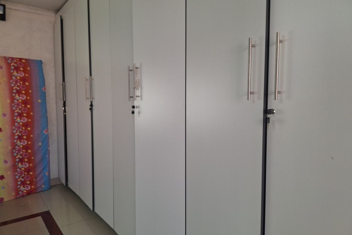 A bedroom featuring extensive floor-to-ceiling built-in cupboards with modern stainless steel handles, providing ample storage space.