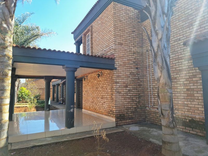 A covered patio area featuring tiled flooring and structural columns, attached to a face-brick exterior wall.