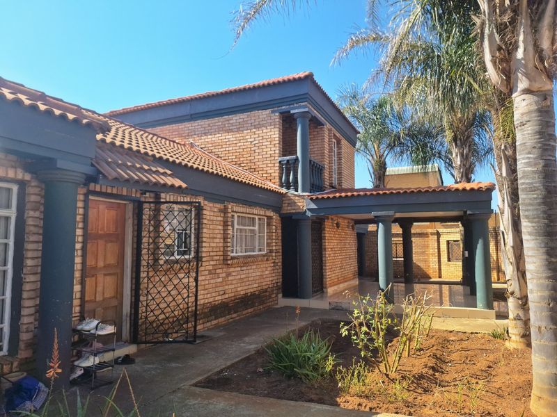 A double-story face brick house featuring a covered patio, balcony with decorative columns, and a front garden area.