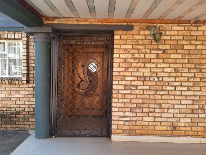 Entrance area featuring a brick facade, a decorative wooden front door with a security gate, and a covered tiled patio.
