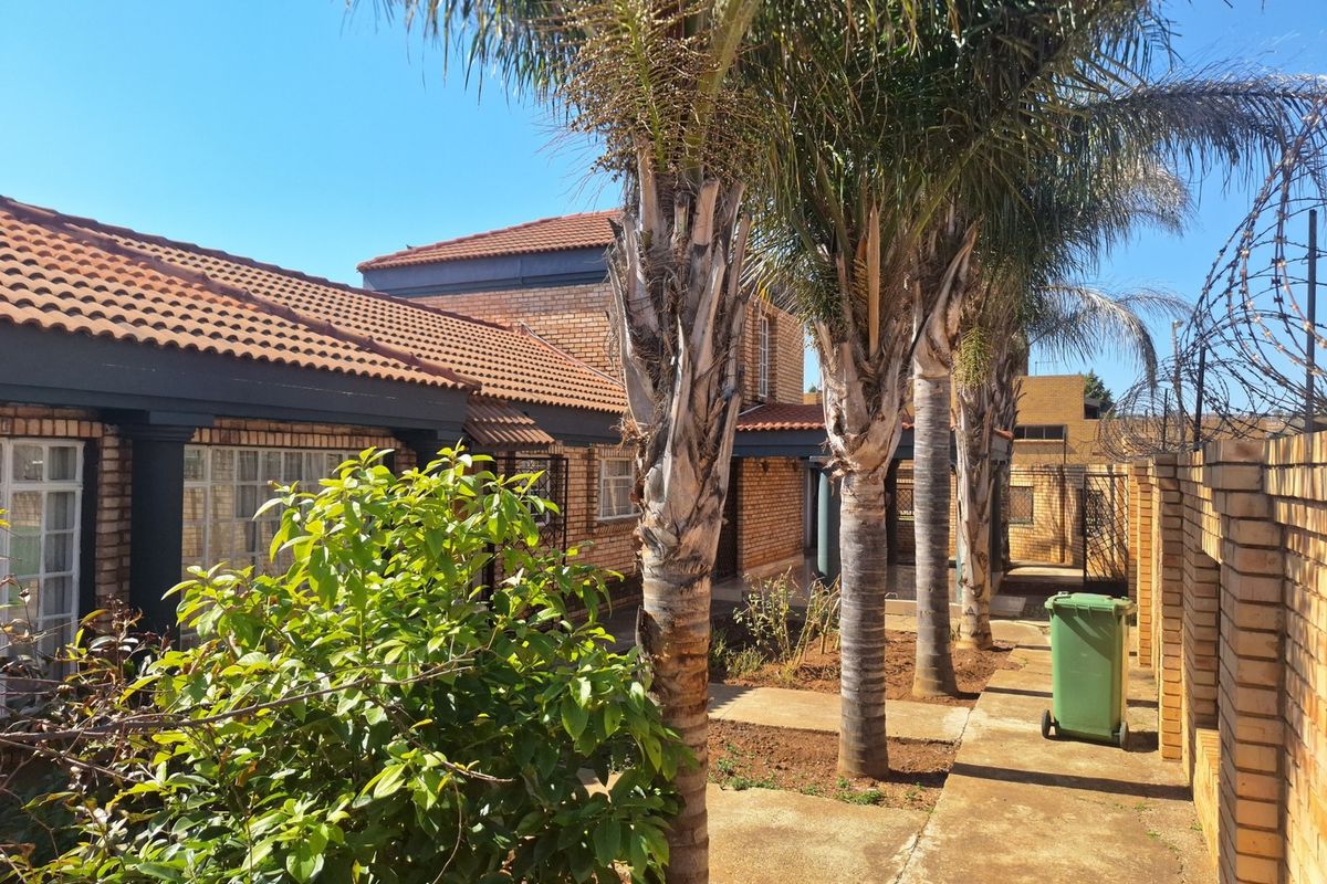 Rear exterior view of the property featuring a brick facade, tiled roof, paved walkway, and established palm trees along the perimeter wall.
