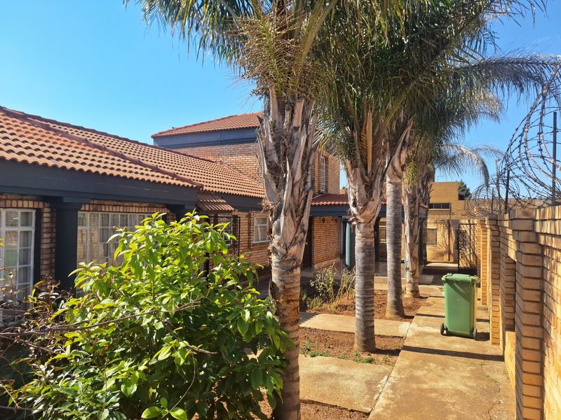 Rear exterior view of the property featuring a brick facade, tiled roof, paved walkway, and established palm trees along the perimeter wall.