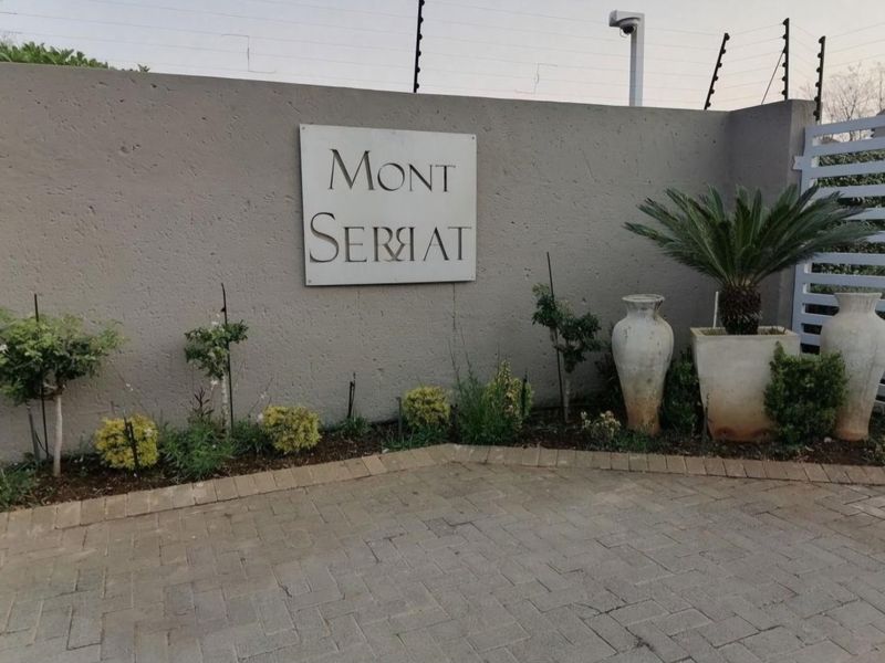 Front entrance view of the Mont Serrat complex featuring a paved driveway, boundary wall with electric fencing, and security surveillance.
