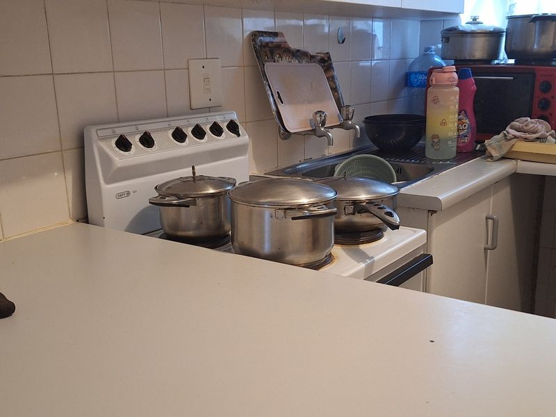 A functional kitchen area featuring a freestanding stove, stainless steel sink, and tiled backsplash with laminate countertops and built-in cabinetry.