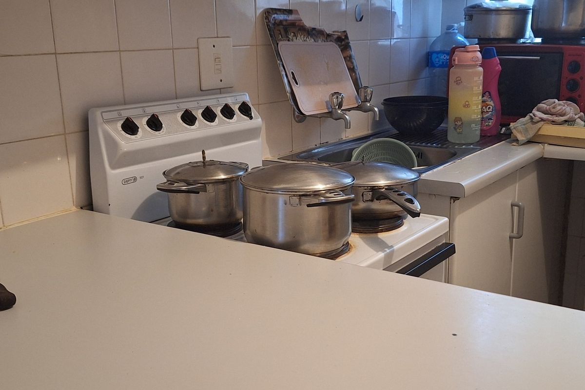 A functional kitchen area featuring a freestanding stove, stainless steel sink, and tiled backsplash with laminate countertops and built-in cabinetry.