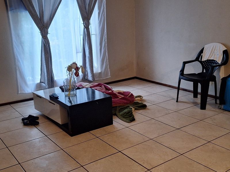A sparsely furnished living area featuring neutral tiled flooring and window treatments, offering a blank canvas for potential interior design updates.