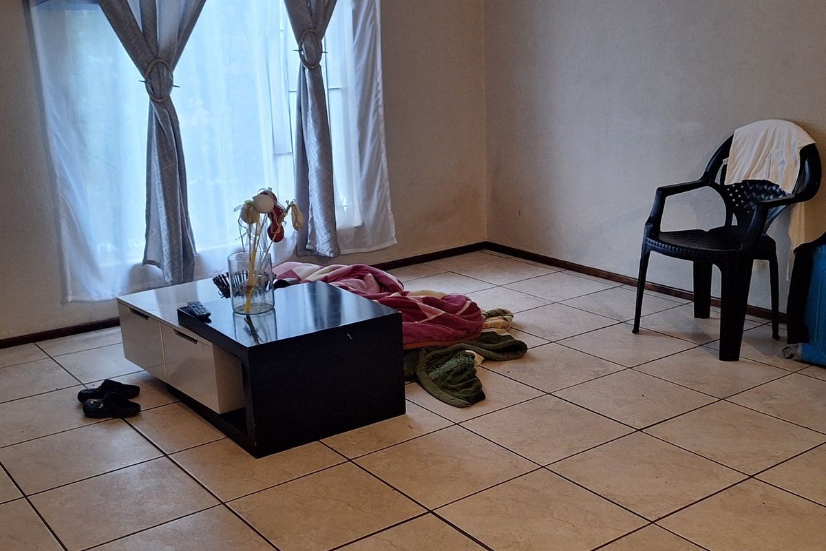A sparsely furnished living area featuring neutral tiled flooring and window treatments, offering a blank canvas for potential interior design updates.