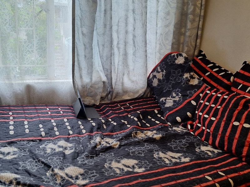 A bedroom interior featuring a window with security bars and curtains.