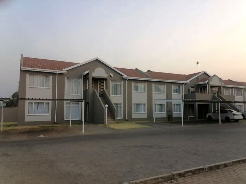 A view of the apartment complex exterior featuring a paved driveway, covered carports, and a multi-unit residential building with a tiled roof.