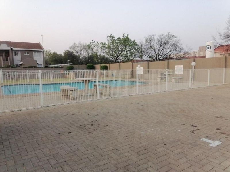 Communal swimming pool area featuring a paved deck, perimeter fencing, and boundary wall, providing a functional outdoor space for residents.