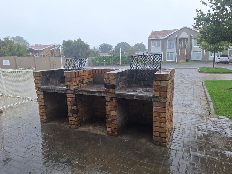 A communal outdoor area featuring a double brick built-in braai station set on a paved surface within an apartment complex.