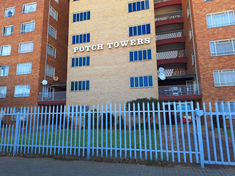 Front elevation of Potch Towers apartment building featuring a brick facade, multiple balconies, and secure perimeter metal fencing.