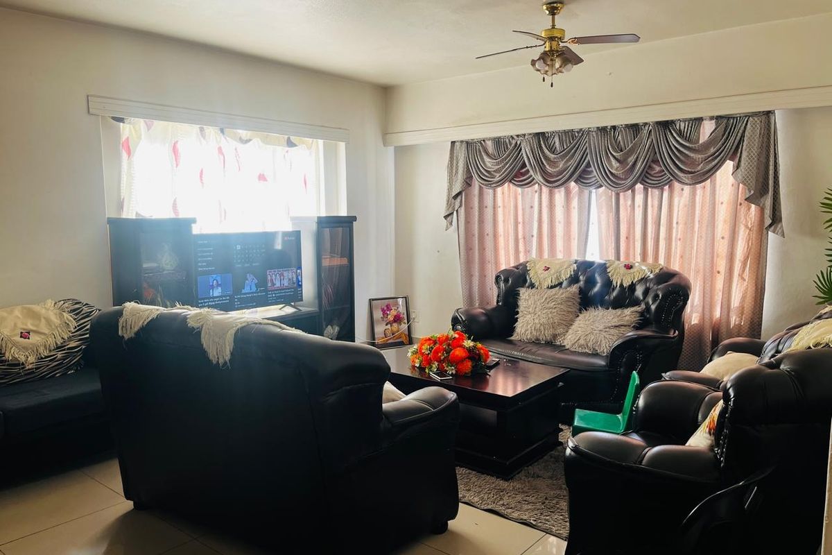 A spacious living room featuring tiled flooring, a ceiling fan, and large windows with decorative curtain pelmets.