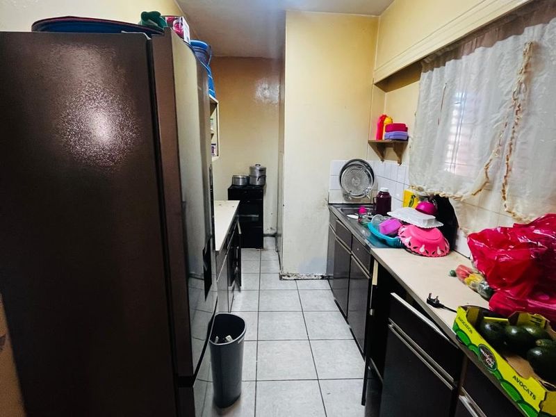 A narrow galley-style kitchen featuring tiled flooring, built-in cabinetry, and a functional sink area, offering potential for modernization and layout optimization.