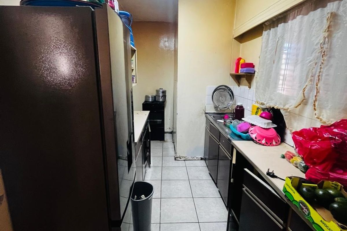 A narrow galley-style kitchen featuring tiled flooring, built-in cabinetry, and a functional sink area, offering potential for modernization and layout optimization.