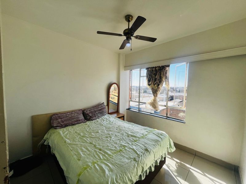 A bedroom featuring tiled flooring, a ceiling fan, and a large window providing natural light and an exterior view.