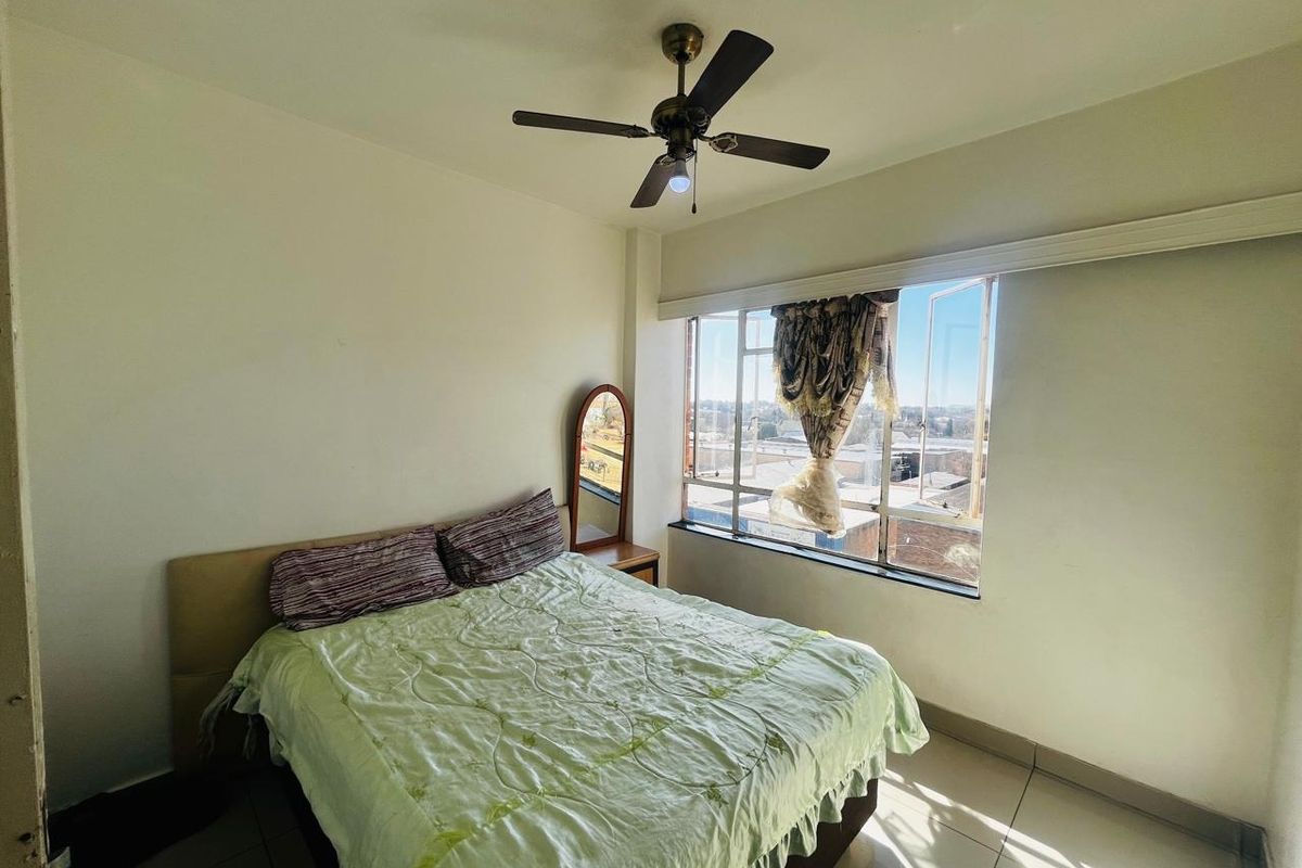 A bedroom featuring tiled flooring, a ceiling fan, and a large window providing natural light and an exterior view.
