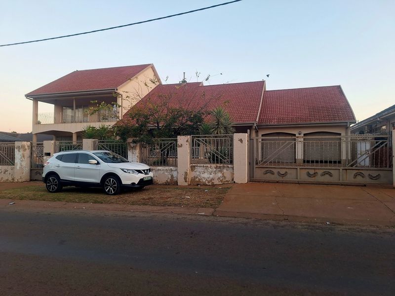 Front elevation of a double-story house featuring a tiled roof, double garage, and a perimeter wall with metal security gates.