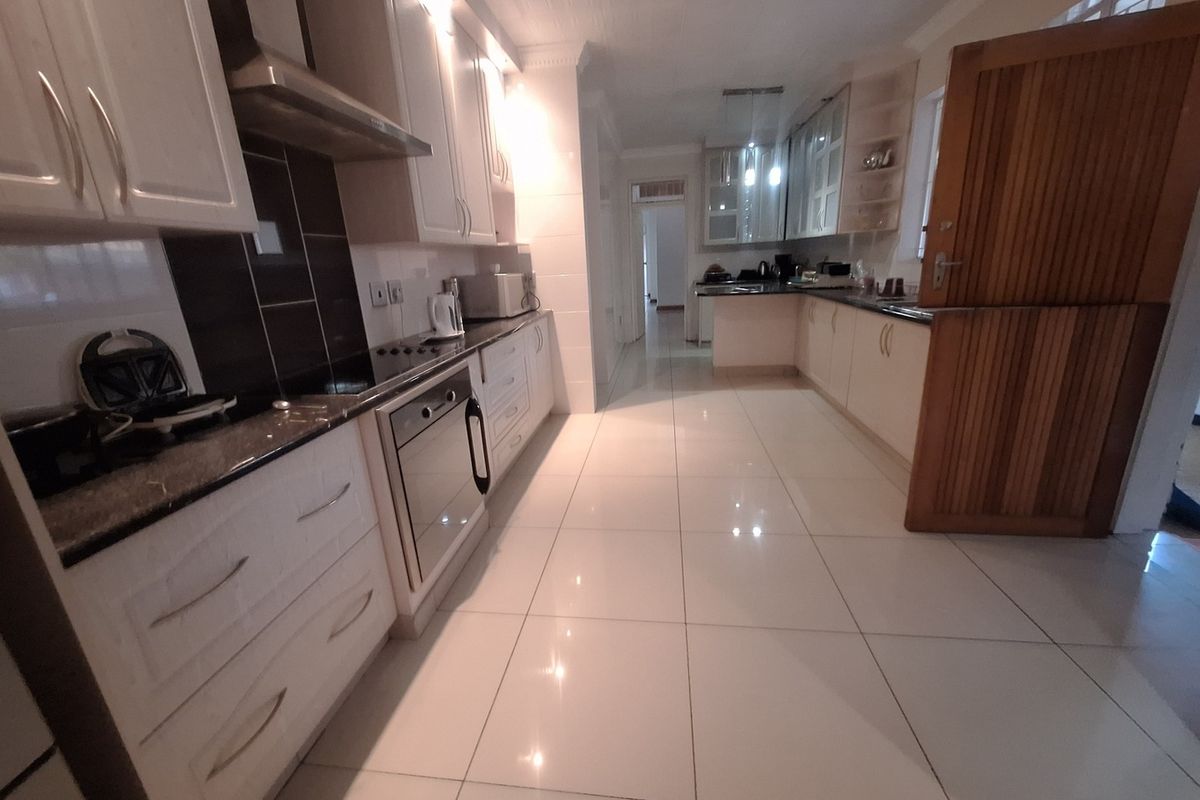 A spacious kitchen featuring white cabinetry, granite countertops, built-in oven, hob, extractor fan, and polished tiled flooring.