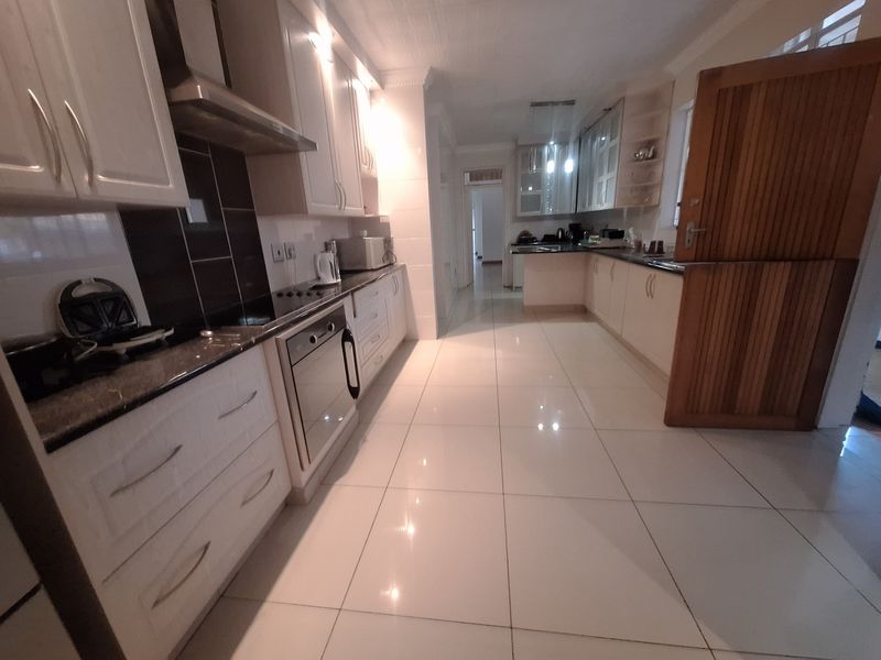 A spacious kitchen featuring white cabinetry, granite countertops, built-in oven, hob, extractor fan, and polished tiled flooring.