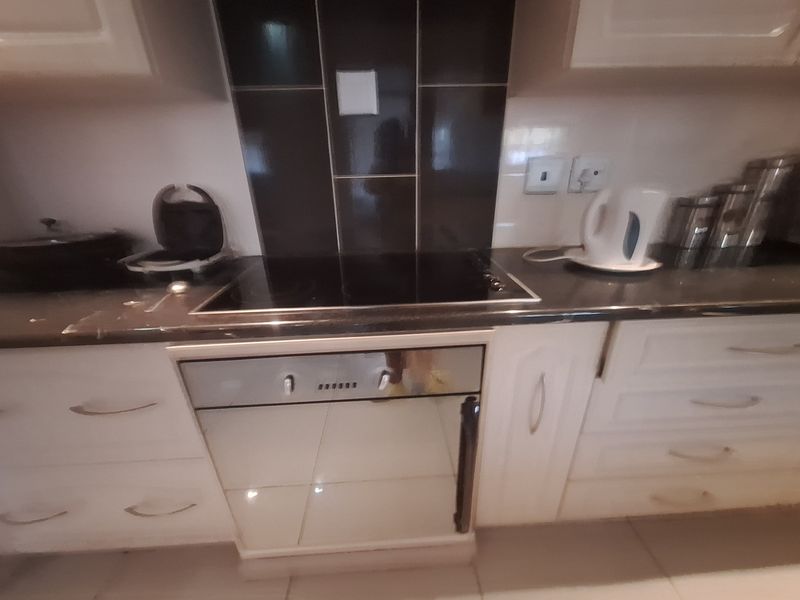 A functional kitchen area featuring a built-in oven, electric hob, dark granite countertops, and white cabinetry with a tiled splashback.