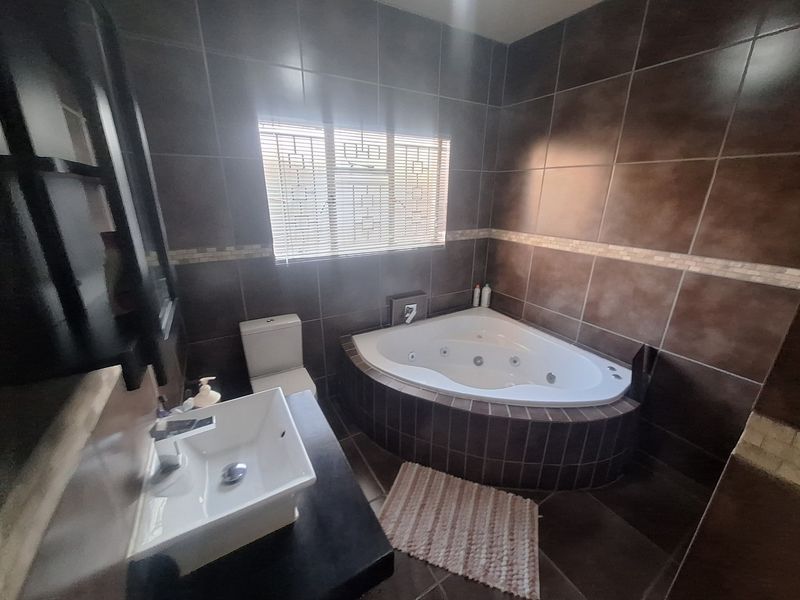 A bathroom featuring a corner spa bath, a modern vessel sink on a vanity, and dark tiled finishes throughout.