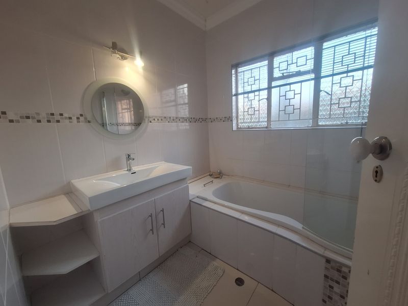 A clean, functional bathroom featuring a vanity with basin, a bathtub with a glass shower screen, and neutral wall tiling.