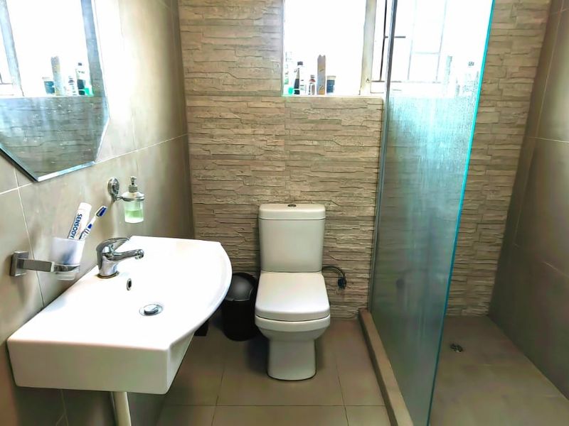 Modern bathroom featuring a wall-mounted basin, toilet, and a walk-in shower with a glass screen and neutral tiled finishes.