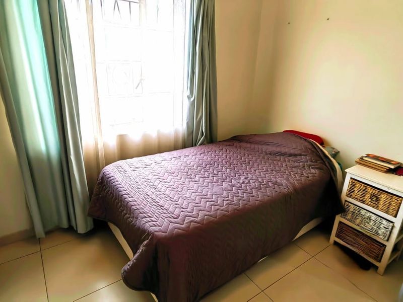 A compact bedroom featuring tiled flooring, a built-in wardrobe, and a window fitted with security bars, providing a functional and well-lit living space.