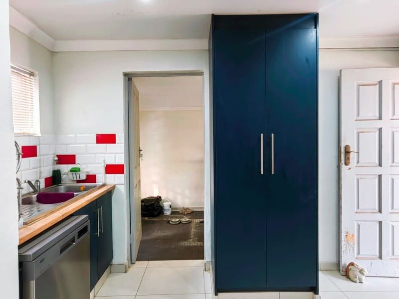 A functional kitchen featuring dark blue cabinetry, a stainless steel sink, subway tile backsplash, and a tall built-in pantry cupboard.