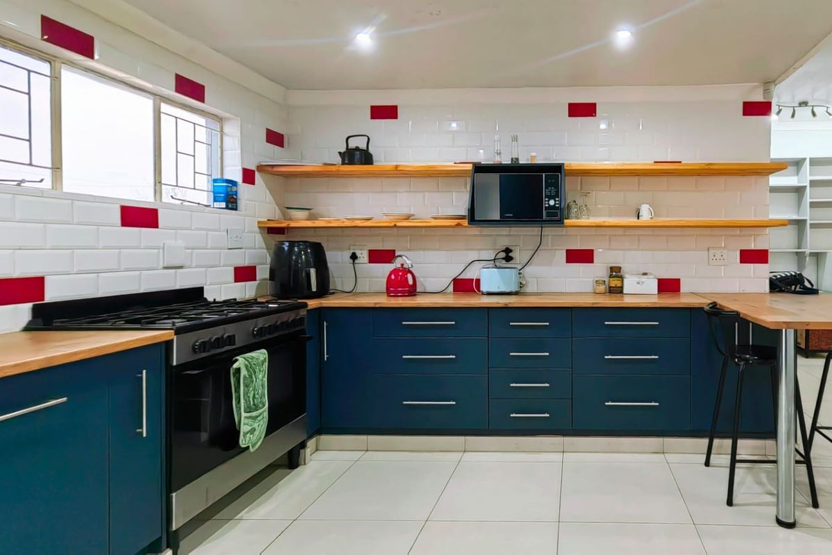 Modern kitchen featuring dark blue cabinetry, wooden countertops, subway tile backsplash with red accents, open shelving, and a gas stove.