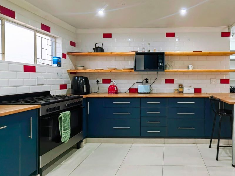 Modern kitchen featuring dark blue cabinetry, wooden countertops, subway tile backsplash with red accents, open shelving, and a gas stove.