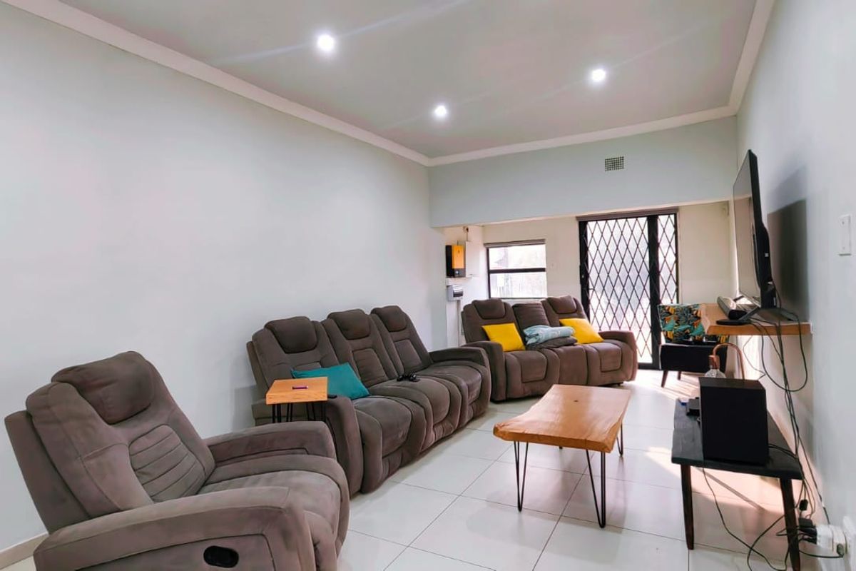 A bright living room featuring tiled flooring, recessed downlighting, and a sliding door with a security gate leading to the exterior.