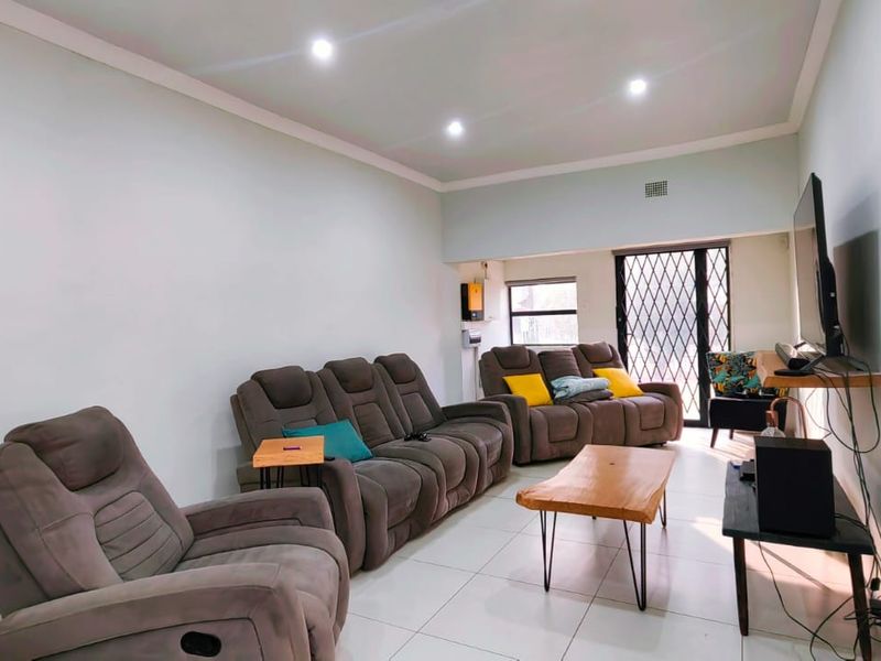 A bright living room featuring tiled flooring, recessed downlighting, and a sliding door with a security gate leading to the exterior.