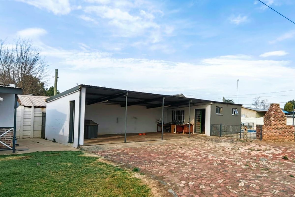 Rear exterior view featuring a large brick-paved area, a covered carport, and a traditional brick built-in braai facility.
