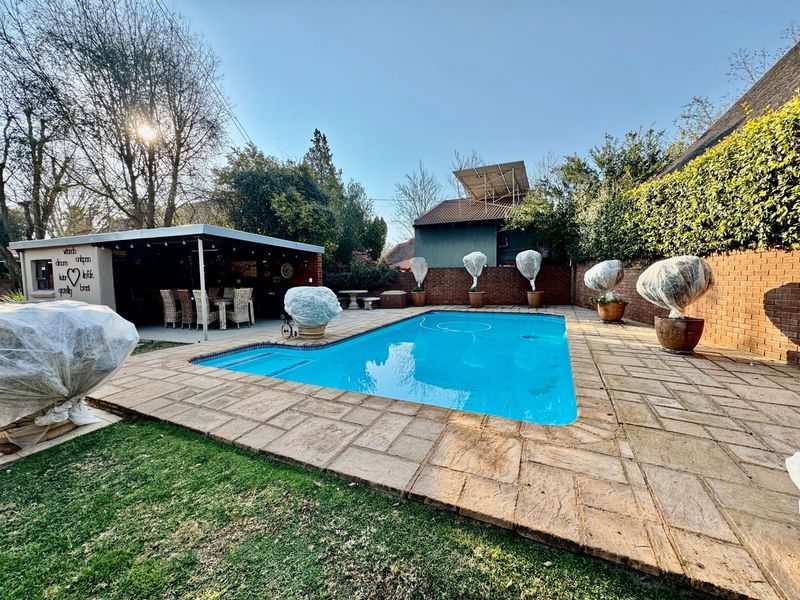 Outdoor pool area featuring a paved deck, a covered patio space, and a brick boundary wall, ideal for outdoor entertaining.