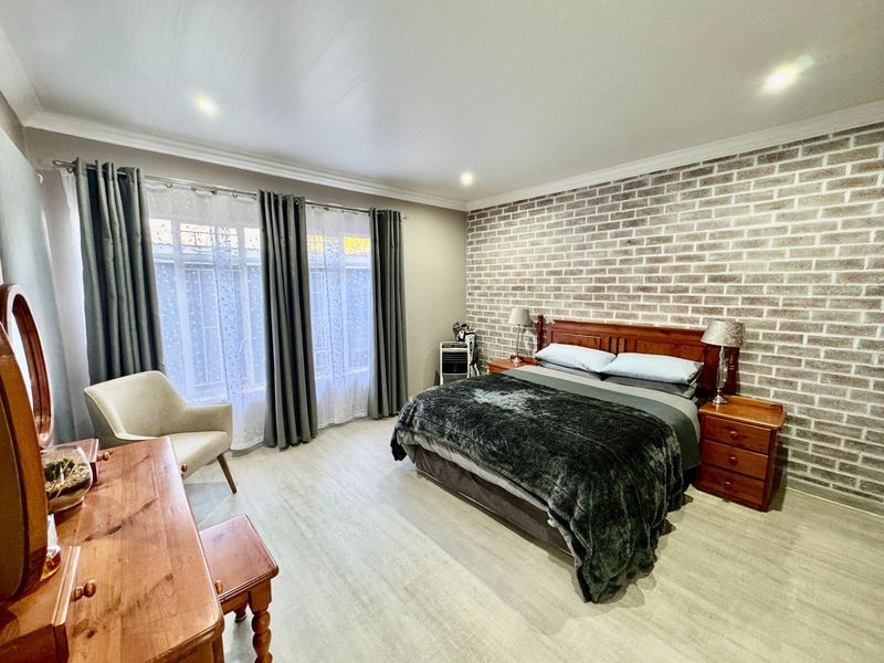 Spacious bedroom featuring a prominent exposed brick feature wall, modern laminate flooring, and recessed downlighting, creating a warm and inviting atmosphere.
