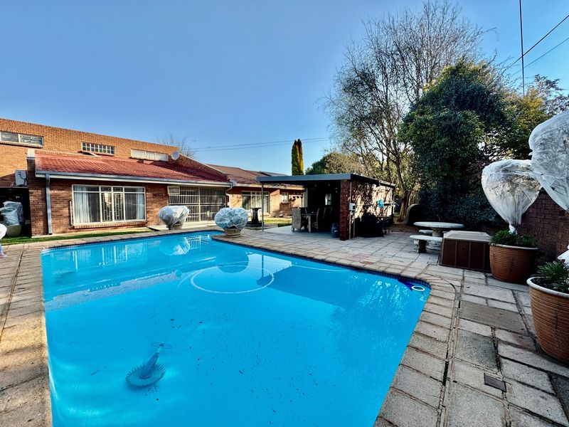 A spacious backyard featuring a swimming pool with a paved deck and an adjacent covered patio area, ideal for outdoor entertaining.