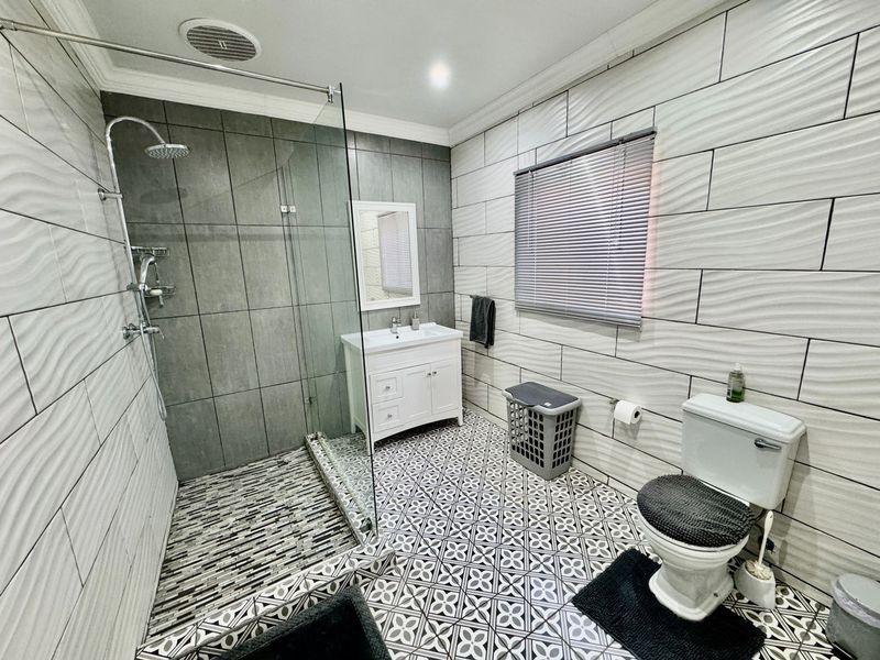Modern bathroom featuring a walk-in shower with glass screen, vanity cabinet with basin, and stylish patterned floor tiles.