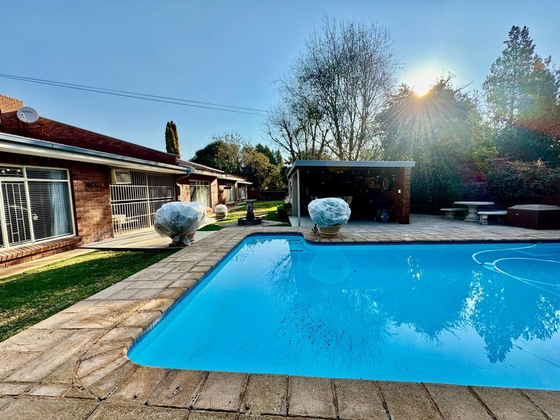 Outdoor pool area featuring a swimming pool with brick coping, adjacent paved patio, and a covered entertainment structure set against a brick house exterior.