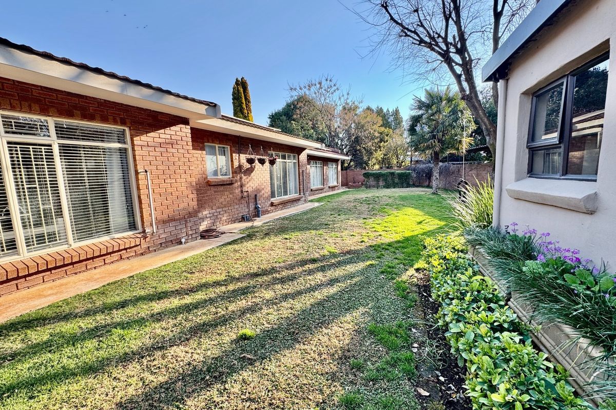 A well-maintained rear garden featuring a brick exterior facade, established lawn, and mature landscaping along the side of the house.