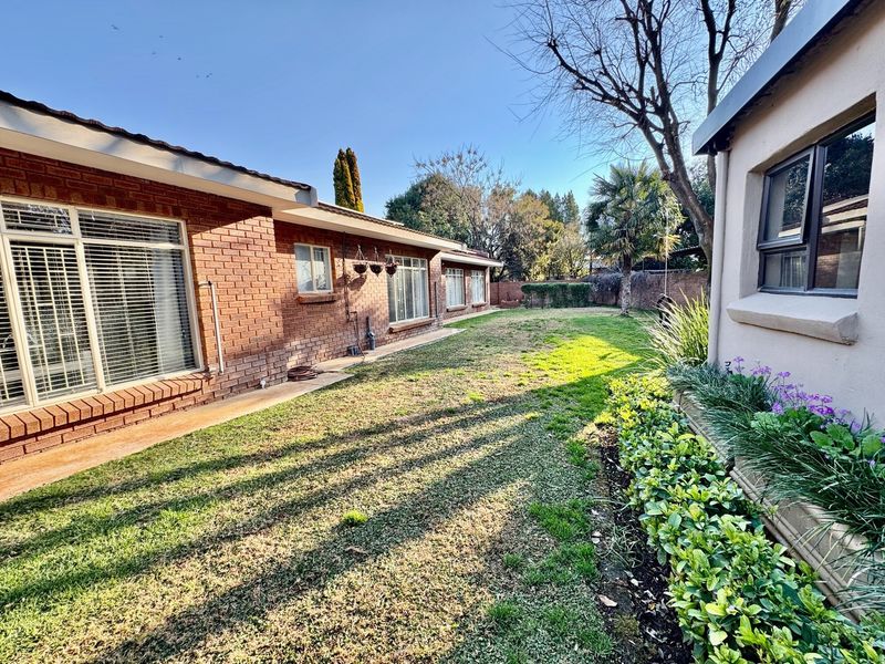 A well-maintained rear garden featuring a brick exterior facade, established lawn, and mature landscaping along the side of the house.