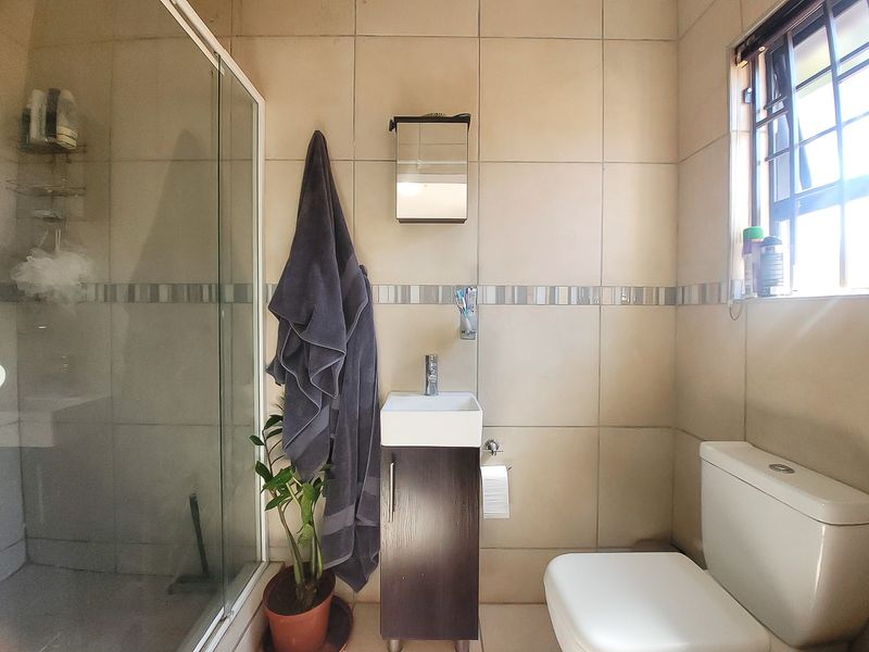 A compact bathroom featuring a shower enclosure, a modern vanity with basin, and a standard toilet, finished with neutral wall tiling.