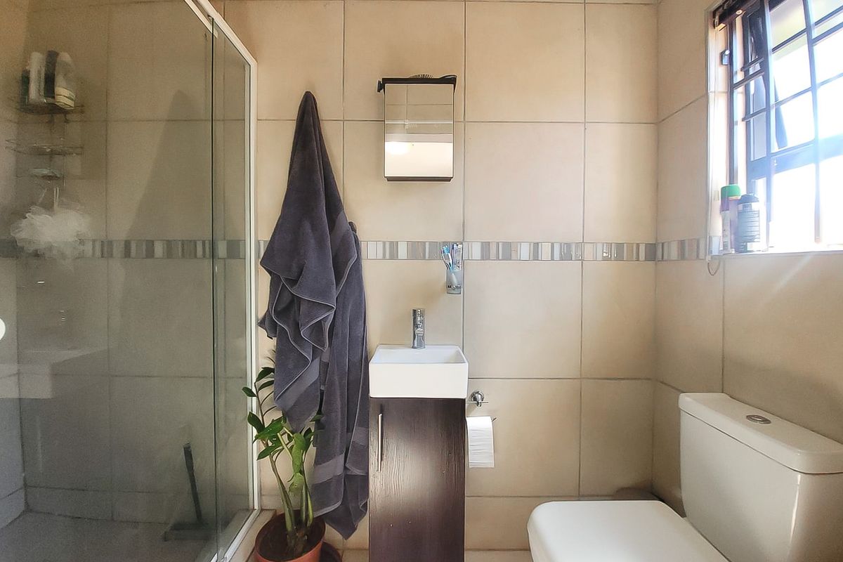 A compact bathroom featuring a shower enclosure, a modern vanity with basin, and a standard toilet, finished with neutral wall tiling.