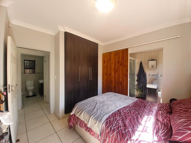 A bedroom featuring built-in cupboards, tiled flooring, and an en-suite bathroom with a sliding door entry.
